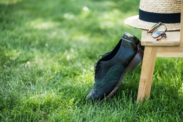 Close up view of arrangement of eyeglasses, black shoes and hat on wooden stairs on green grass — Stock Photo