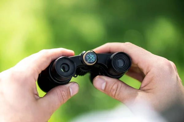 Cropped shot of man holding binoculars on blurred green background — Stock Photo