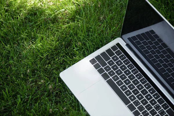 Vista de cerca de la computadora portátil abierta con pantalla en blanco sobre hierba verde - foto de stock