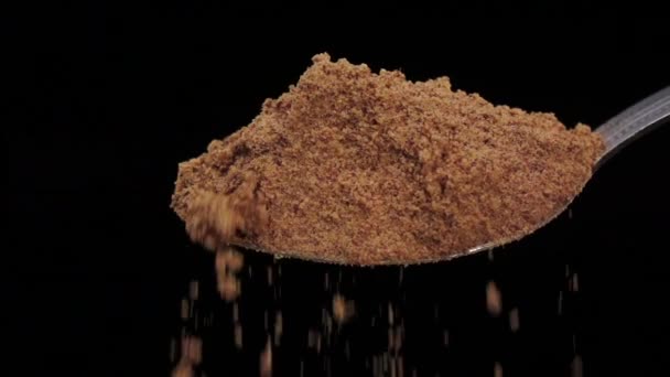 Poudre de curcuma tombant de la cuillère en argent, studio de fond noir, ralenti 