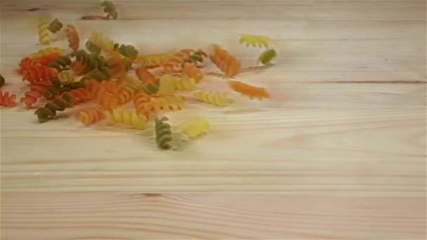 Gekleurde rauwe pasta valt op een houten tafel. Slow motion — Stockvideo