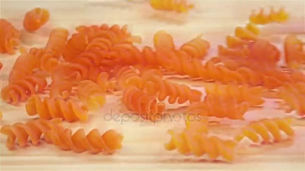 Spiraal vorm rode pasta valt op houten tafel, slow-motion — Stockvideo