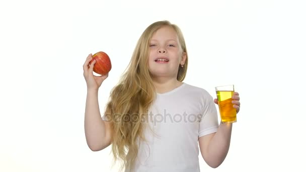 Bebês menina bebe suco de um copo e segura uma maçã. Fundo branco — Vídeo de Stock