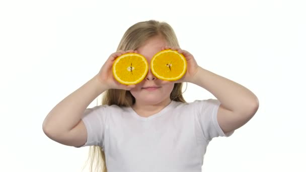 La niña sosteniendo una rebanada de naranja cierra los ojos y las curvas. Fondo blanco — Vídeos de Stock