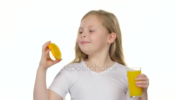 Κοριτσάκι κατέχει μία φέτα πορτοκάλι και γλείφει και πίνει χυμό πορτοκάλι. Λευκό φόντο — Αρχείο Βίντεο