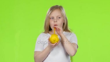 Küçük kız bir limon tutan ve bir saman limon suyu içme. Yeşil ekran