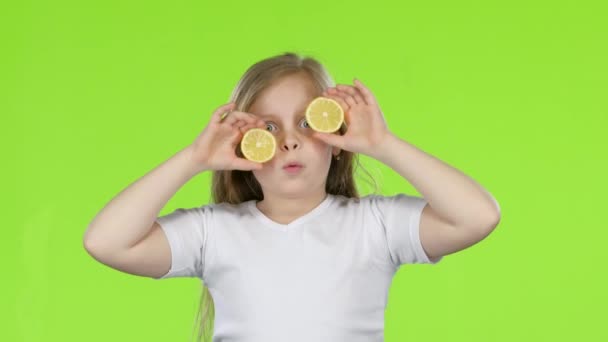 Kid girl closes her eyes with a lemon and shows different emotions, licks it and croaks. Green screen — Stock Video