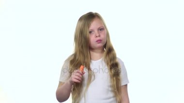 Küçük kız bir havuç yiyor ve baş parmak işareti gösterir. Beyaz arka plan. Ağır çekim