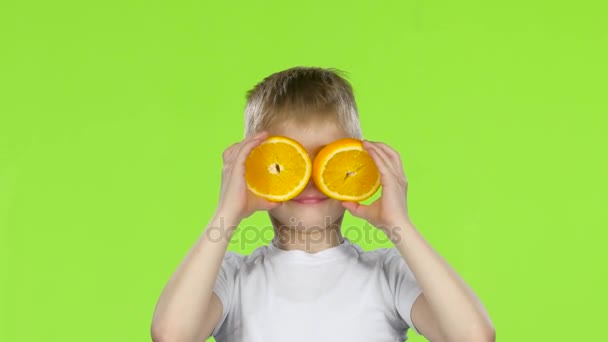 El niño sostiene una rebanada de naranja y hace varias muecas. Pantalla verde — Vídeo de stock