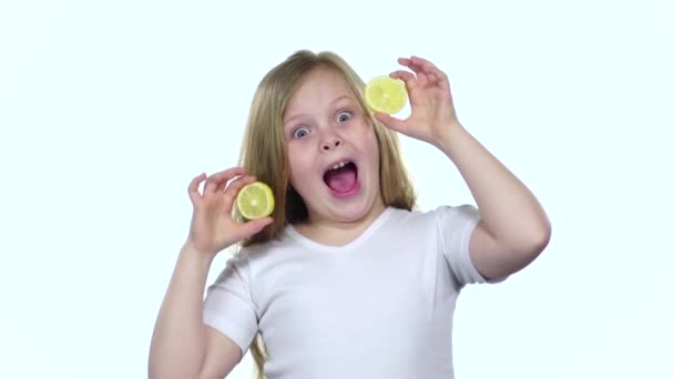 Children closes her eyes with a lemon and shows different emotions, licks it and croaks. White background. Slow motion — Stock Video