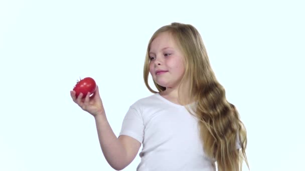 Baby looks at a tomato, admires it and shows a thumbs up. White background. Slow motion — Stock Video
