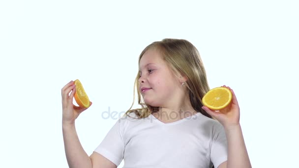 La niña sosteniendo una rebanada de naranja cierra los ojos y las curvas. Fondo blanco. Movimiento lento — Vídeo de stock