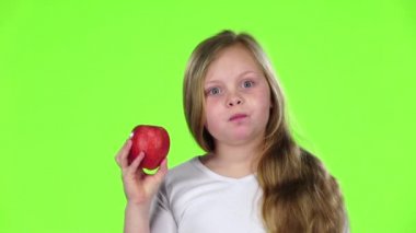 Küçük kız bir elma ısırıkları ve baş parmak işareti gösterir. Yeşil ekran. Ağır çekim