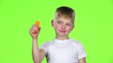 Küçük çocuk bir havuç elinde tutar ve onu ısırır. Yeşil ekran. Ağır çekim