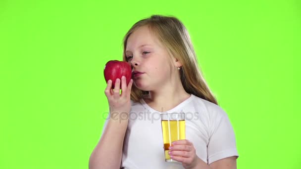 Маленькая девочка пьет сок из стакана и держит яблоко. Зеленый экран. Медленное движение — стоковое видео