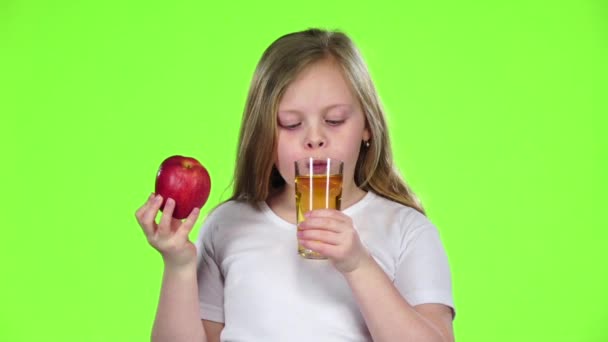 Mała dziewczynka pije sok ze szkła i trzyma jabłko. Zielony ekran. Zwolnionym tempie — Wideo stockowe