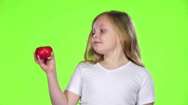 La niña mira un tomate, lo admira y muestra un pulgar hacia arriba. Pantalla verde. Movimiento lento — Vídeos de Stock