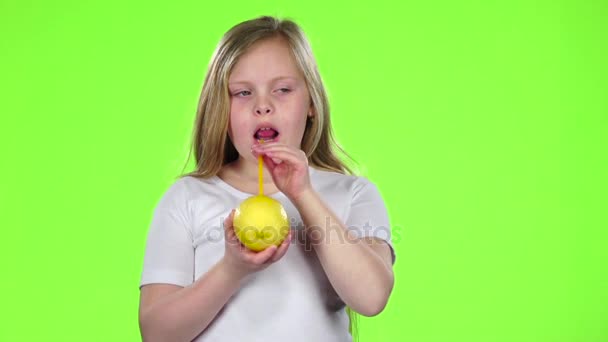 Little girl is holding a lemon and drinking juice from a lemon through a straw. Green screen. Slow motion — Stock Video