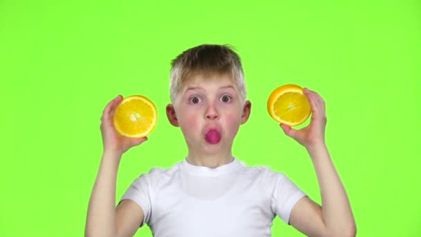 Menino segura uma fatia de laranja e faz várias caretas. Tela Verde. Movimento lento — Vídeo de Stock