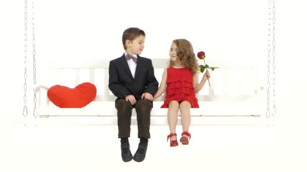 Ein kleiner Junge und ein kleines Mädchen sitzen auf einer Schaukel, ein netter Plausch. weißer Hintergrund — Stockvideo