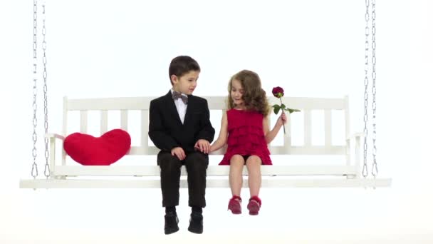 Ein kleiner Junge und ein kleines Mädchen sitzen auf einer Schaukel, ein netter Plausch. weißer Hintergrund. Zeitlupe — Stockvideo