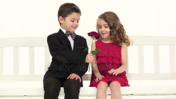 Liten pojke ger en ros till sin flickvän, hon accepterar och ler. Vit bakgrund. Slow motion. Närbild — Stockvideo