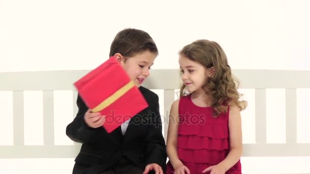 Liten pojke tar ett par byxor och ger flickan i återvänder hon kysser honom på kinden. Vit bakgrund. Slow motion. Närbild — Stockvideo