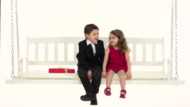 Children ride on a white swing tell each other secrets in the ear. White background. Slow motion. Close up — Stock Video