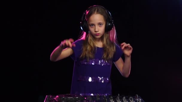 Дівчина-підліток діджей в навушниках грає за обертовий стіл. Чорний фон — стокове відео