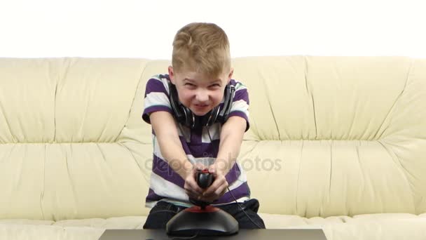 Ребенок играет с джойстиком в онлайн-игру, сидя на диване — стоковое видео
