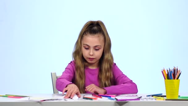 Liten flicka finner rätt penna och ritar. Vit bakgrund. Slow motion — Stockvideo