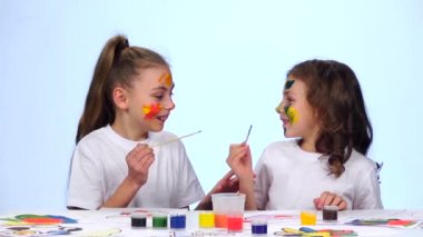 İki küçük kız masaya oturup, püsküllü yüzlerinde resim. Beyaz arka plan. Ağır çekim