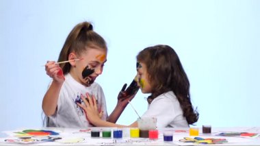 Giysilerini için boyalar uygulamadan masada oturan çocuk. Beyaz arka plan. Ağır çekim