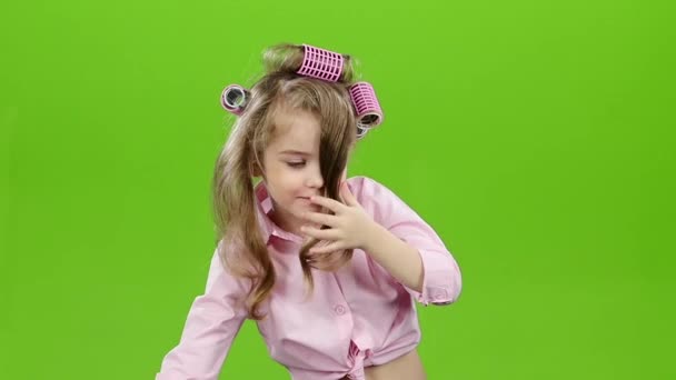 Ребенок в бигудях показывает язык на камере. Зеленый экран. Медленное движение — стоковое видео