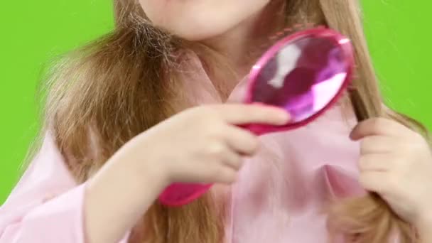 Little girl is holding a comb and combing her long, silky hair. Green screen. Slow motion — Stock Video