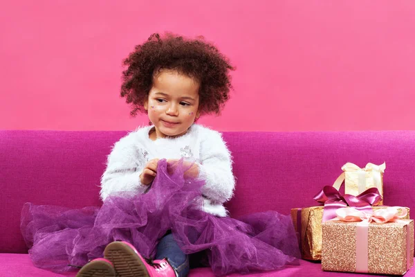 Een klein meisje met veel geschenkdozen die op de bank zitten. — Stockfoto