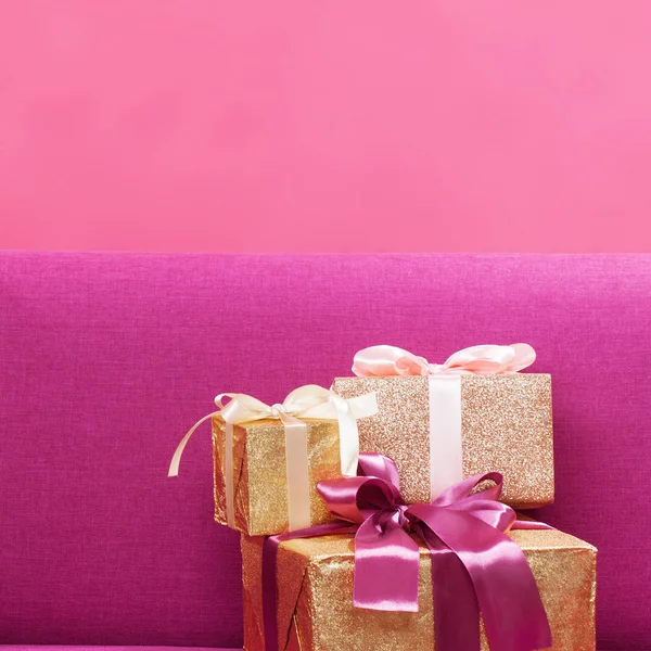 Tři zlaté dárkové krabice na růžovém pozadí — Stock fotografie