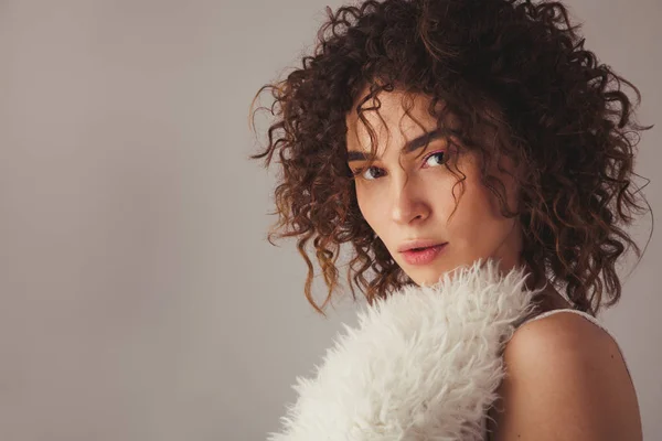 Beautiful woman with curly hair in furry coat against gray backg — ストック写真
