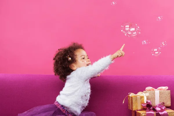 Cute little girl with a lot of gift boxes sitting on sofa and ca — Stock Photo, Image