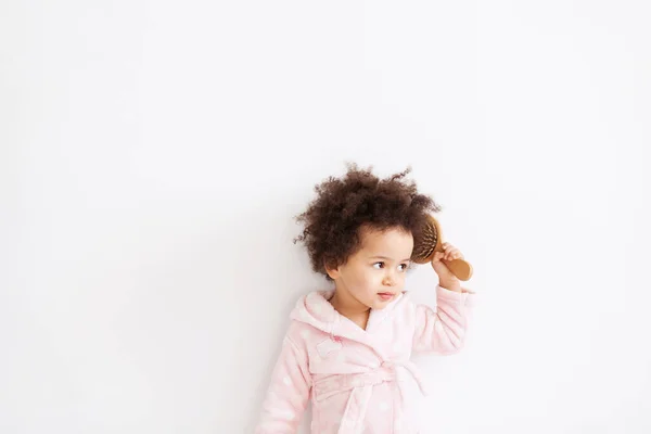 Menina bonito em roupão de banho macio escovando seu cabelo encaracolado — Fotografia de Stock