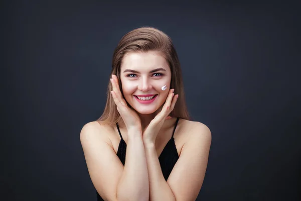 Schöne Frau mit glatter, gesunder Haut, die ihr Gesicht eincremt — Stockfoto