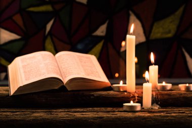 İncil ve eski meşe ahşap bir masa üzerine de mum. Güzel vitray windows arka plan. Din kavramı.