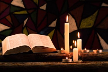 İncil ve eski meşe ahşap bir masa üzerine de mum. Güzel vitray windows arka plan. Din kavramı.