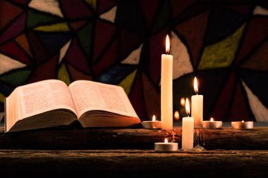 İncil ve eski meşe ahşap bir masa üzerine de mum. Güzel vitray windows arka plan. Din kavramı.