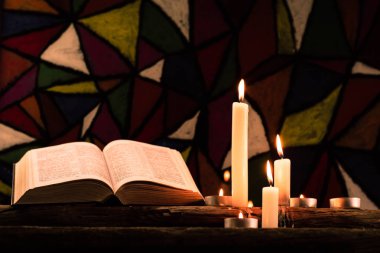 İncil ve eski meşe ahşap bir masa üzerine de mum. Güzel vitray windows arka plan. Din kavramı.