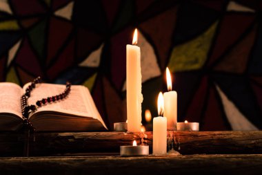 İncil haç ve boncuk eski meşe ahşap bir masa üzerinde bir mum. Güzel vitray windows arka plan. Din kavramı.