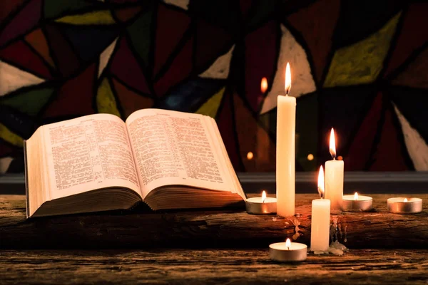 聖書の十字架と古いオークの木のテーブルにキャンドルのビーズ 美しいステンド グラスの窓の背景 宗教概念 — ストック写真