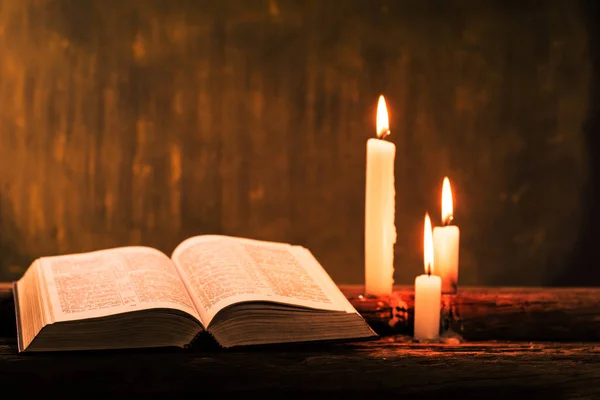 Bible crucifix and beads with a candle on a old oak wooden table.  Beautiful gold background.Religion concept.