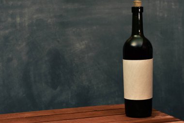 Eski bir ahşap masa üzerinde beyaz dokusal etiket ile kırmızı şarap şişesi. Güzel koyu arka plan