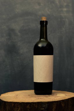 Eski bir ahşap masa üzerinde beyaz dokusal etiket ile kırmızı şarap şişesi. Güzel koyu arka plan